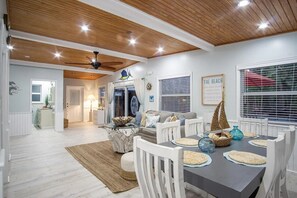 A dining area with a wooden ceiling, white walls, and a view of the beach through the window.