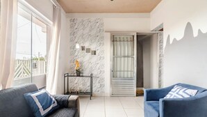 Una sala de estar moderna con un sofá, un sillón azul, una pared de mármol y un ventanal que da a un balcón.