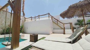 A poolside area with a wooden swing, a small trash bin, and a lounge chair.