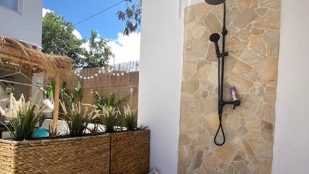 A modern outdoor shower area with a stone wall, a woven planter with plants, and a wooden deck.
