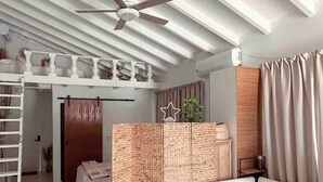 Une chambre avec un lit superposé, un ventilateur de plafond, une cloison en osier et une table de chevet.
