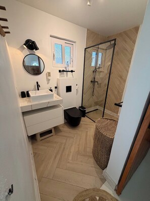 A modern bathroom with a white vanity, a round mirror, a shower with a glass door, and a herringbone-patterned floor.