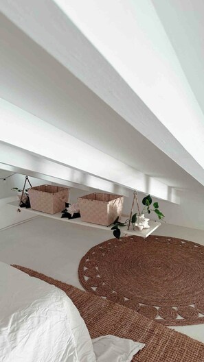 A room with a large woven rug, a hanging plant, and a basket on the floor.