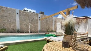 Un espace piscine avec une pelouse artificielle, une table en osier et un panier, ainsi qu’un mur en pierre.