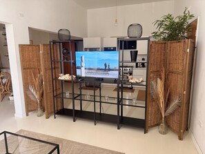 Een moderne woonkamer met een televisie, rieten meubels en een keukenhoek.