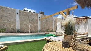 Een zwembadgedeelte met kunstgras, een rieten lounge stoel en een stenen muur.