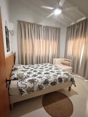 Een slaapkamer met een bed, een plafondventilator en gordijnen.