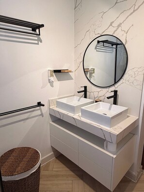 Een badkamer met twee witte wasbakken, een ronde spiegel en een wand met marmerprint.
