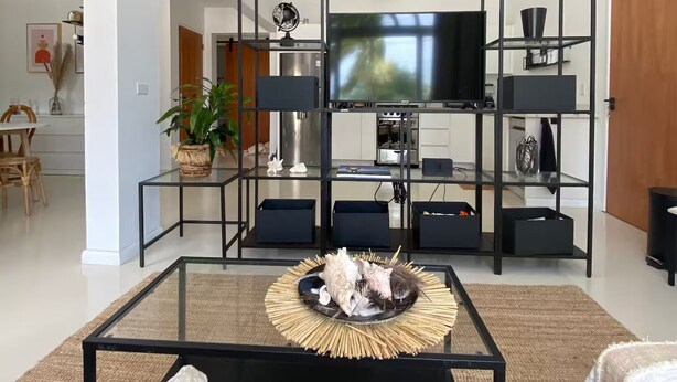 Een moderne woonkamer met een zwarte salontafel, een flatscreen televisie en zwarte wandplanken.