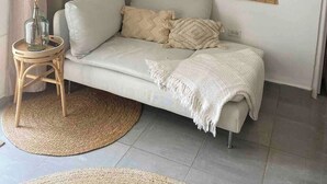 A living room with a sofa, a woven blind, a vase with dried plants, and a round woven rug. - Palm Beach VacaySuites - Garden Suite - Poolside (Palm Beach)