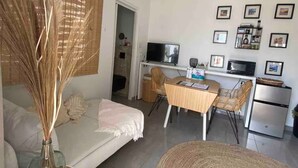 A modern living room with a sofa, dining table, and chairs. There is a TV, a refrigerator, and framed pictures on the wall. - Palm Beach VacaySuites - Garden Suite - Poolside (Palm Beach)