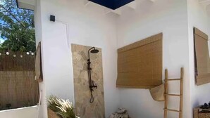 A covered outdoor area with a stone shower, a wooden ladder, and a woven basket planter. - Palm Beach VacaySuites - Garden Suite - Poolside (Palm Beach)