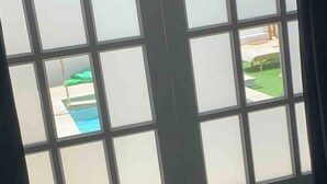 A view through a window with a view of a swimming pool and a green lawn. - Palm Beach VacaySuites - Garden Suite - Poolside (Palm Beach)