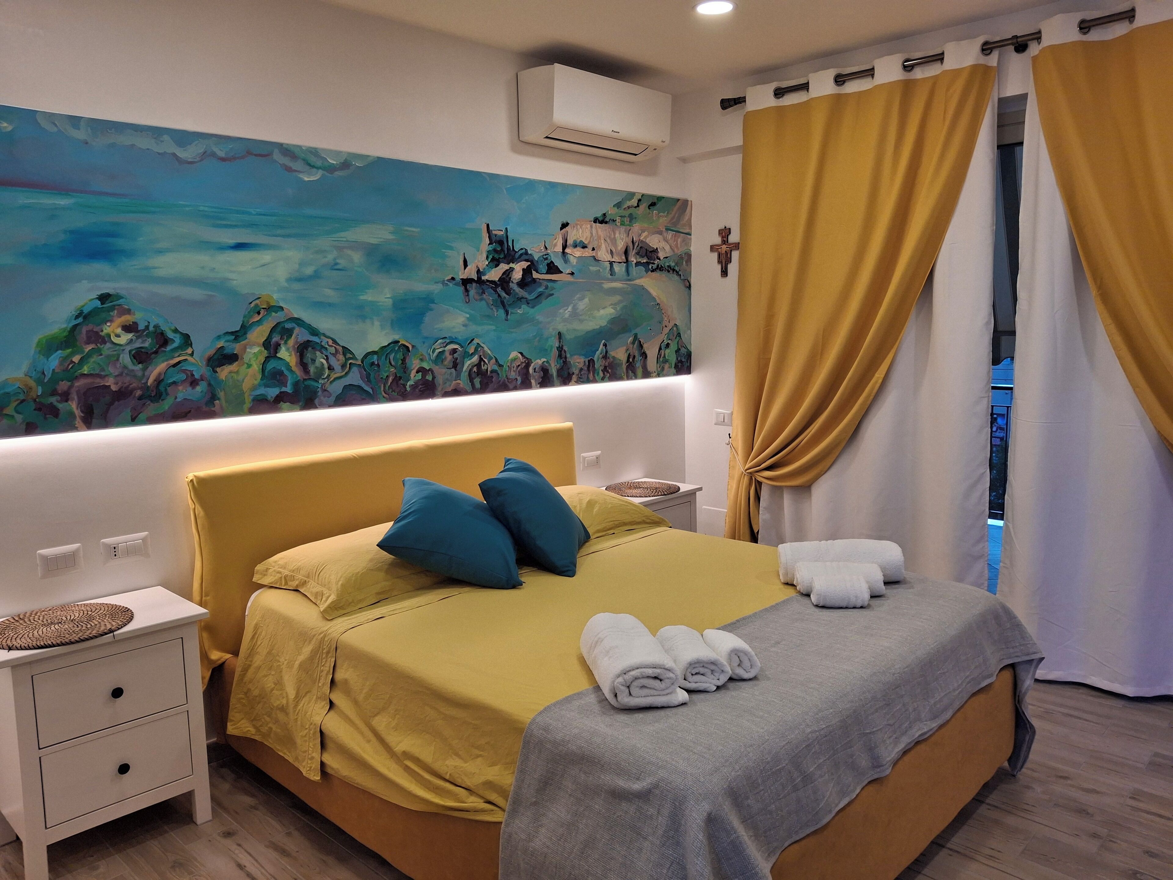 Een hotelkamer met een bed, nachtkastje, schilderij aan de muur en een raam met gordijnen.