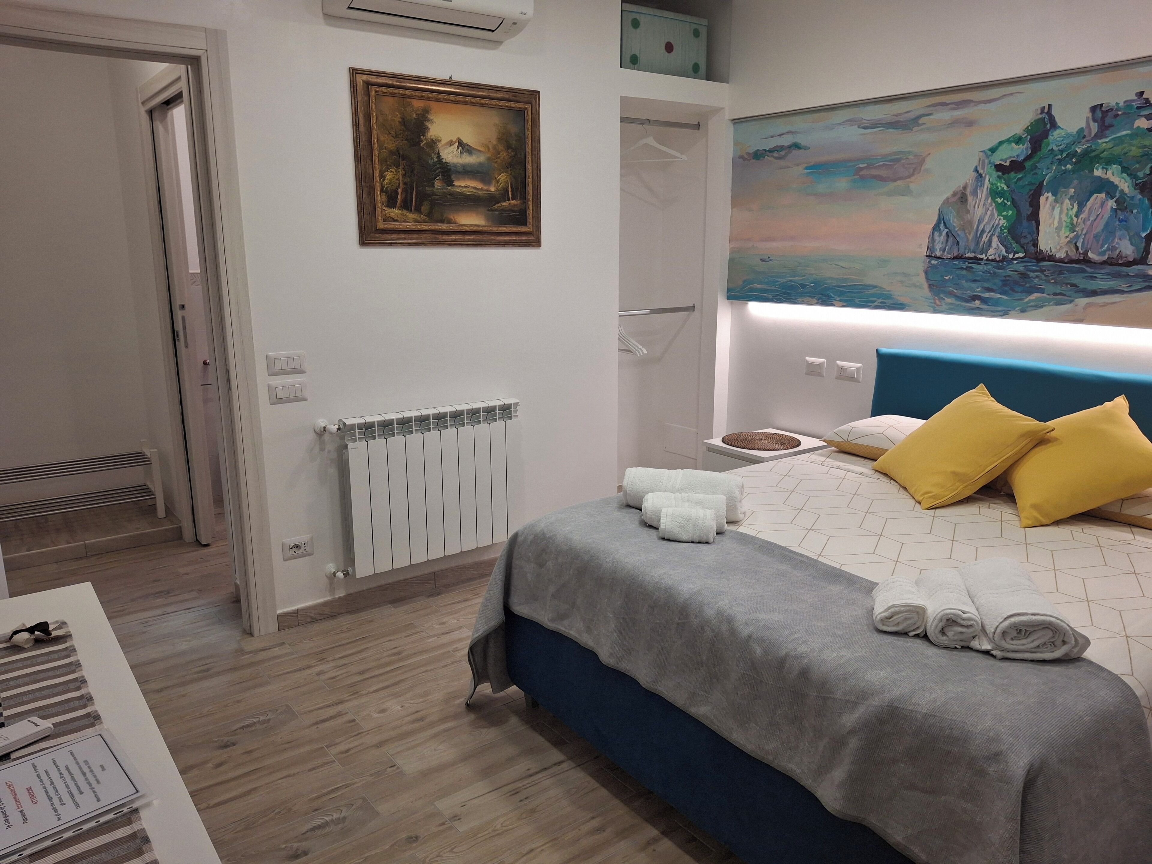 A bedroom with a bed, towels, a painting, and a radiator.