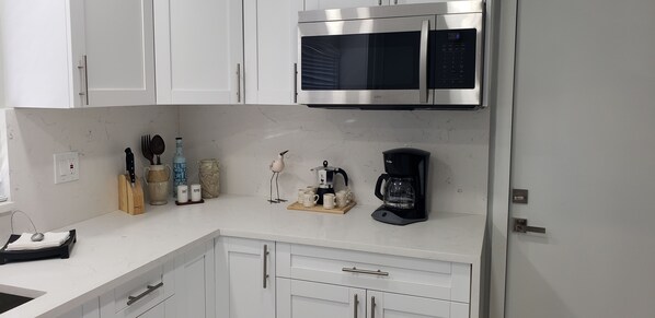 A modern kitchen with white cabinets, a stainless steel microwave, a coffee maker, and various kitchen utensils.