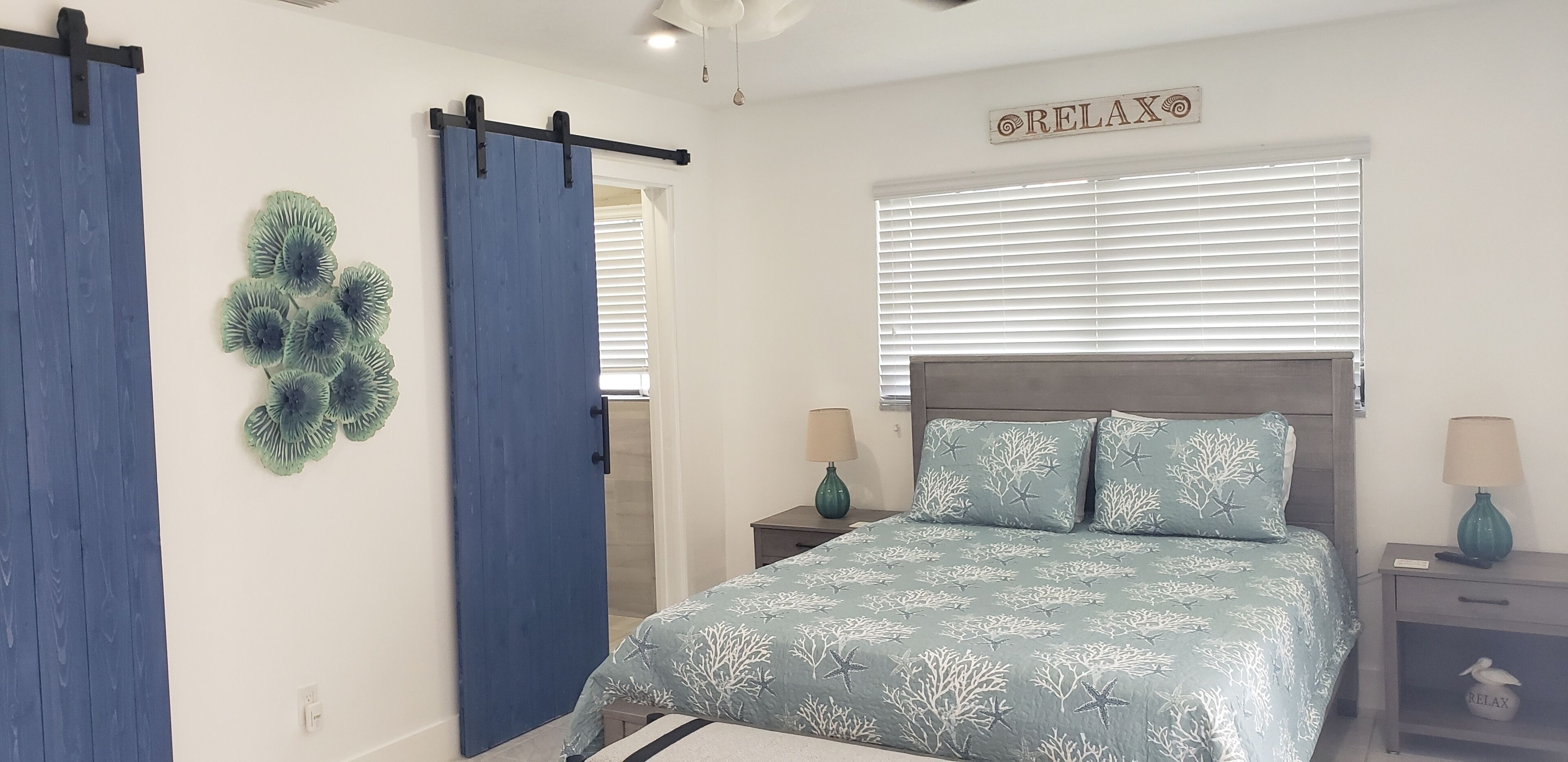 Une chambre à coucher comprenant un lit, deux tables de chevet, un panneau décoratif fixé au mur et une porte coulissante.