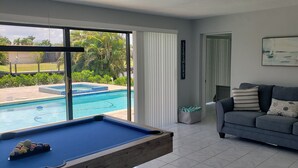A living room with a pool table, a gray sofa, and a painting on the wall. - Cozy, bright, and spaciuos WF home with pool, dock, pool table & more. (Cape Coral)