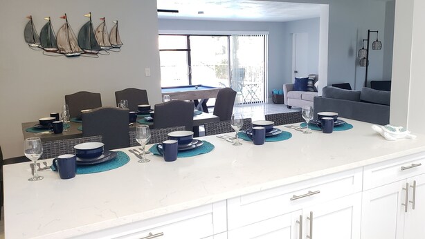 A modern kitchen with white cabinets, a marble countertop, and a dining area with a pool table. - Cozy, bright, and spaciuos WF home with pool, dock, pool table & more. (Cape Coral)