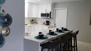 A modern kitchen with white cabinets, a microwave, and a dining area with black chairs and teal placemats. - Cozy, bright, and spaciuos WF home with pool, dock, pool table & more. (Cape Coral)