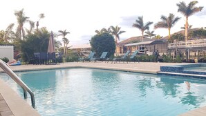 A pool area with lounge chairs, palm trees, and a building in the background. - Cozy, bright, and spaciuos WF home with pool, dock, pool table & more. (Cape Coral)