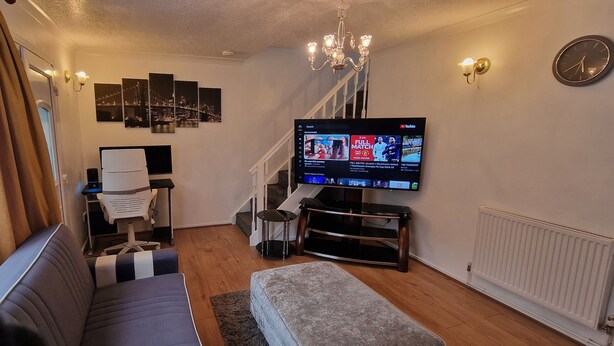 Ein Wohnzimmer mit einer Couch, einem an der Wand befestigten Fernseher, einem Schreibtisch mit Stuhl und einer Treppe.