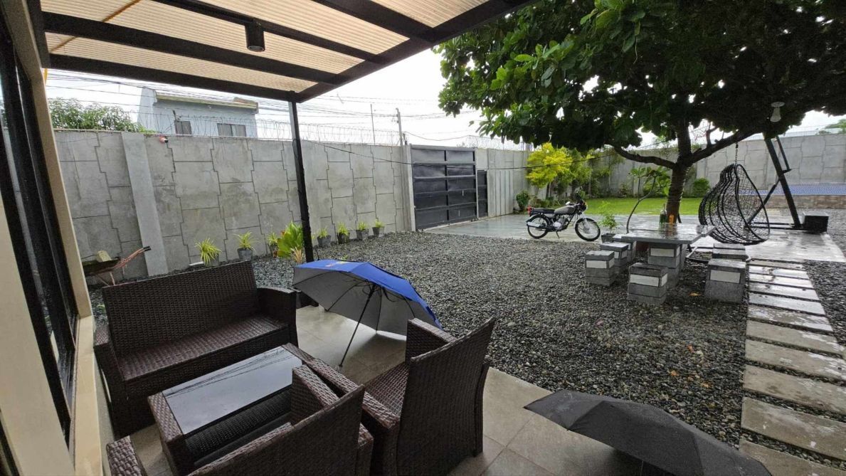 Een overdekt terras met rieten meubels, een tafel en een blauwe parasol.