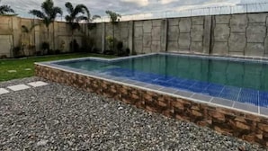Ein rechteckiger Pool mit Steinrand, umgeben von einer Steinmauer und einem Metallzaun.