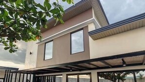Ein modernes, zweistöckiges Haus mit überdachter Terrasse und Gartenmöbeln.