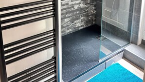 Un área de ducha moderna con puerta de vidrio, azulejos grises y un panel de control.