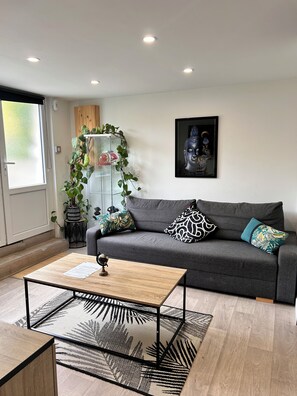 A modern living room with a grey sofa, patterned cushions, a wooden coffee table, and a glass cabinet with plants. - Quiet accommodation facing the forest 10 min from Orly airport near Paris (Athis-Mons)