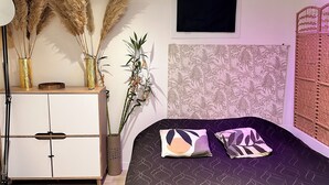 Un dormitorio con cama, mesita de noche, lámpara y plantas decorativas.