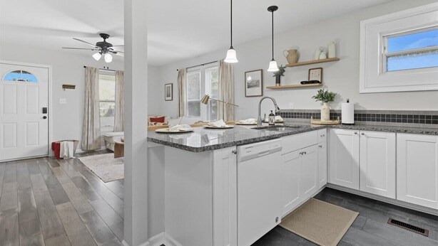 A modern kitchen with white cabinets, a granite countertop, pendant lighting, and a window with a view.