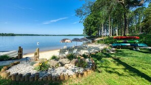 Un patio junto al lago con mobiliario exterior, kayaks y una terraza de madera.