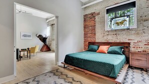 Un dormitorio con cama, una mesita de noche de madera, una ventana con un vitral de un caballo, una pared de ladrillo y una puerta que da a otra habitación.