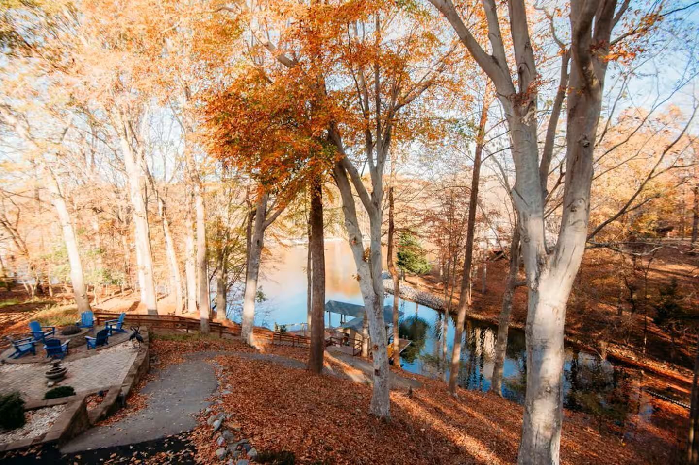 A serene outdoor setting with a wooden deck, blue chairs, and a stone pathway leading to a rustic cabin by a lake.