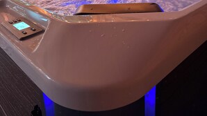 Ein Whirlpool mit Bedienfeld und LED-Beleuchtung, umgeben von Holzbalken und einer Brüstung.