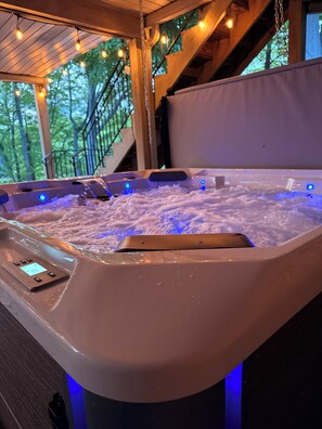 Un bain à remous doté d’un panneau de commande et de lumières LED, entouré de poutres en bois et d’une rambarde.