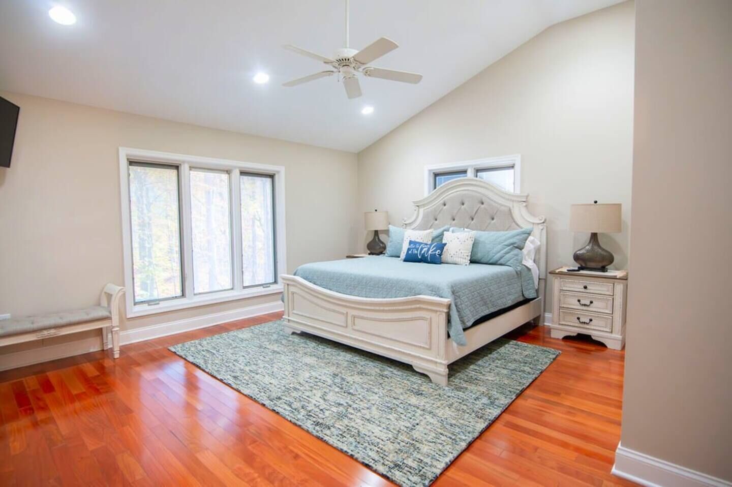 A bedroom with a bed, nightstands, a ceiling fan, and large windows.