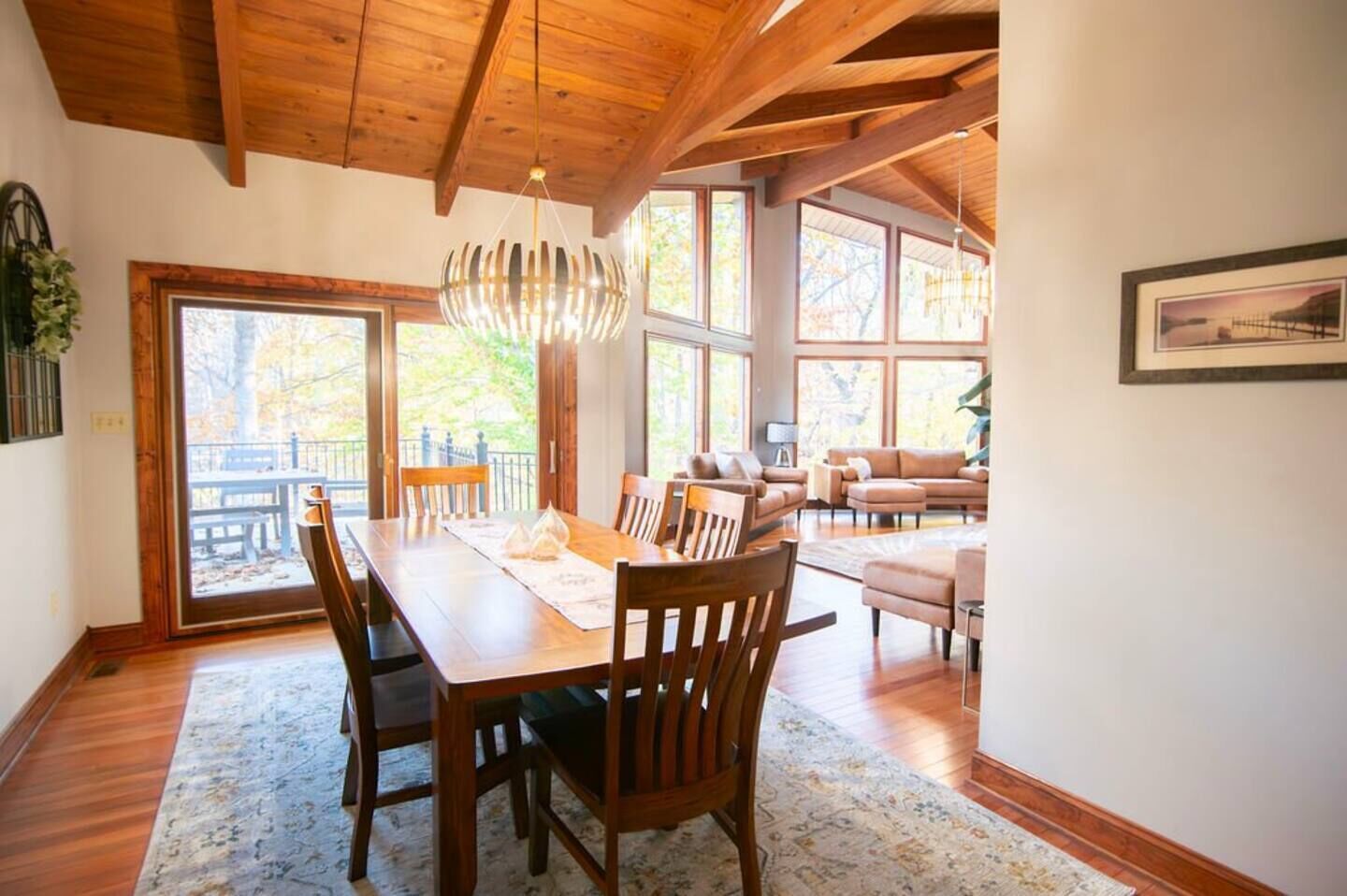 Un espace repas avec une table et des chaises en bois, de grandes fenêtres et une vue sur l’extérieur.