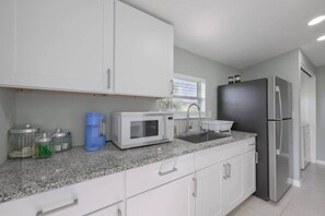 Eine moderne Küche mit weißen Schränken, einer Granit-Arbeitsplatte, einer Mikrowelle, einem Spülbecken und einem Kühlschrank.