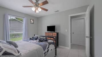 Une chambre à coucher avec un lit, un ventilateur de plafond, une commode, un téléviseur et une porte.