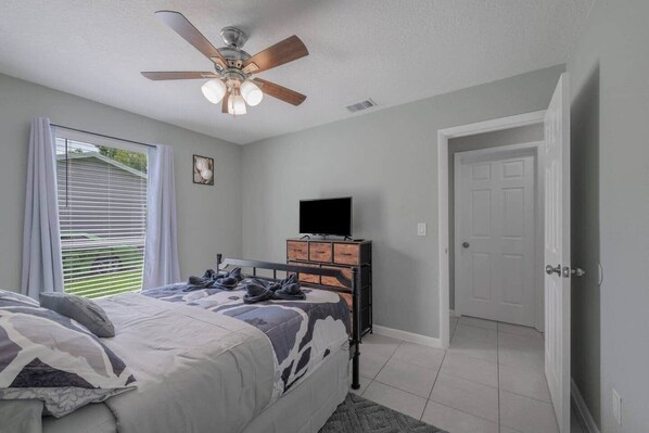 Une chambre à coucher avec un lit, un ventilateur de plafond, une commode, un téléviseur et une porte.