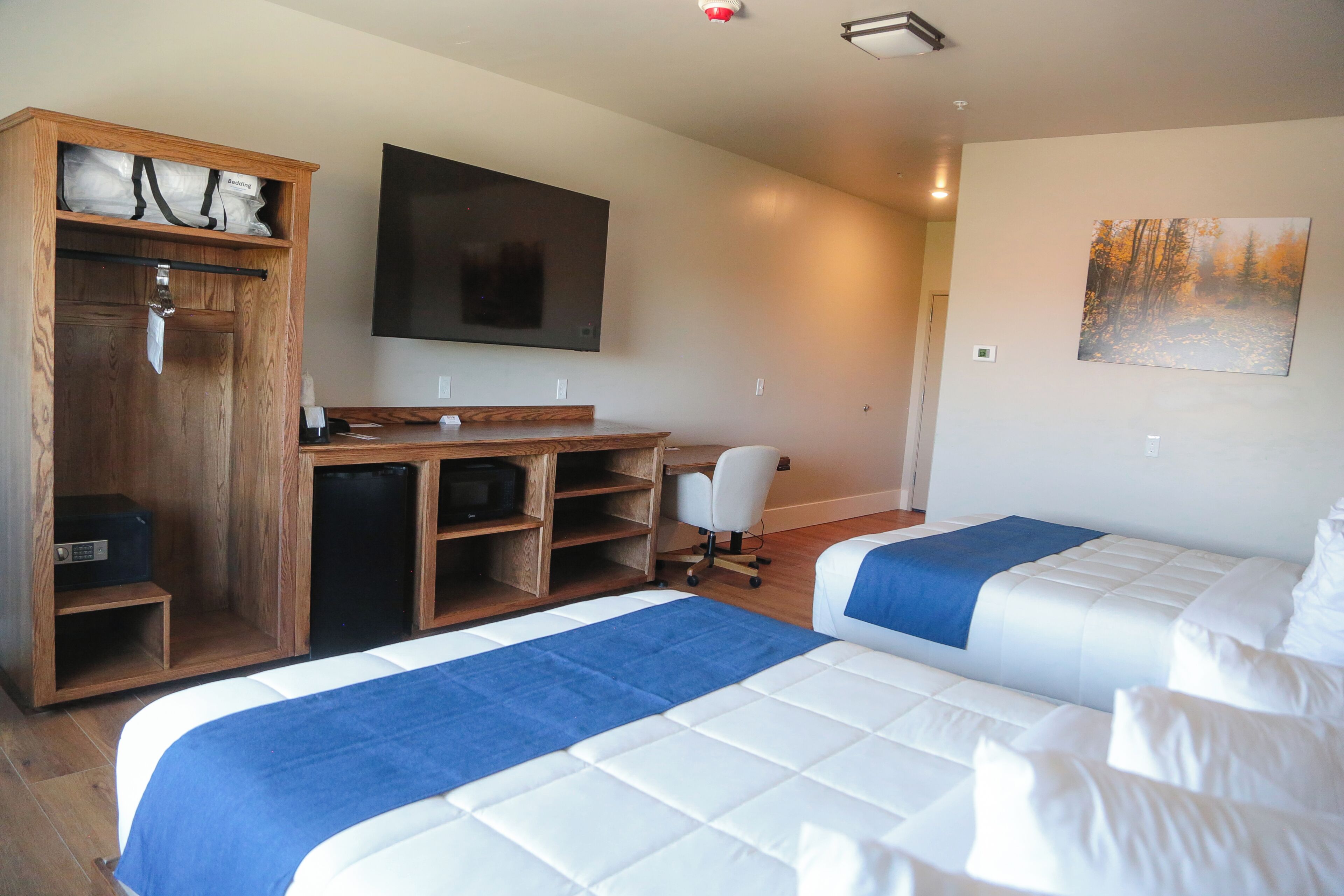 A hotel room with two beds, a desk, a chair, a TV, and a wardrobe.