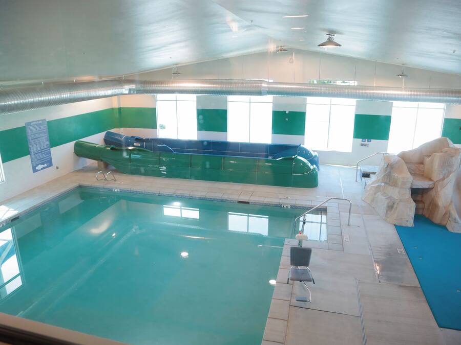 Piscina interna com trampolim, placa de regras de segurança e um elemento decorativo com formato de rocha.