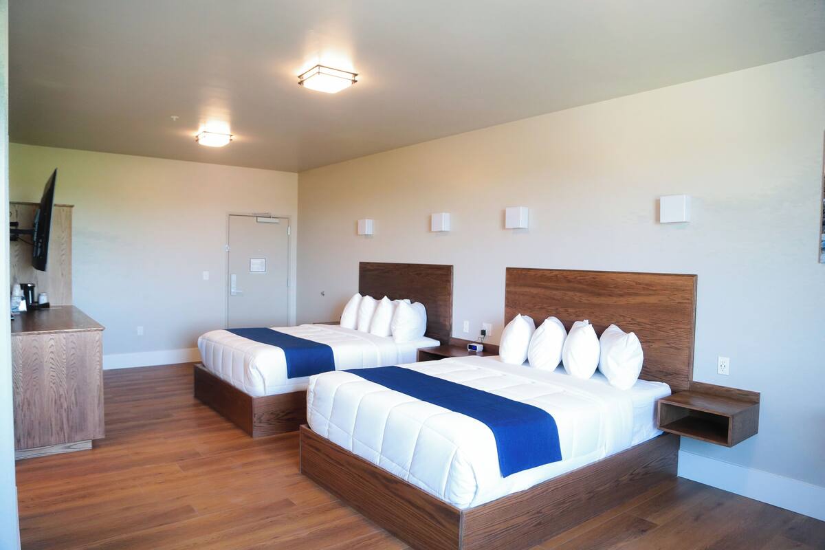 Une chambre d’hôtel avec deux lits, une commode en bois, un téléviseur à écran plat et une petite table de chevet.