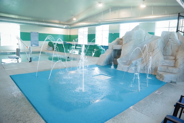 An indoor swimming pool with a blue floor, water features, and a rock formation.