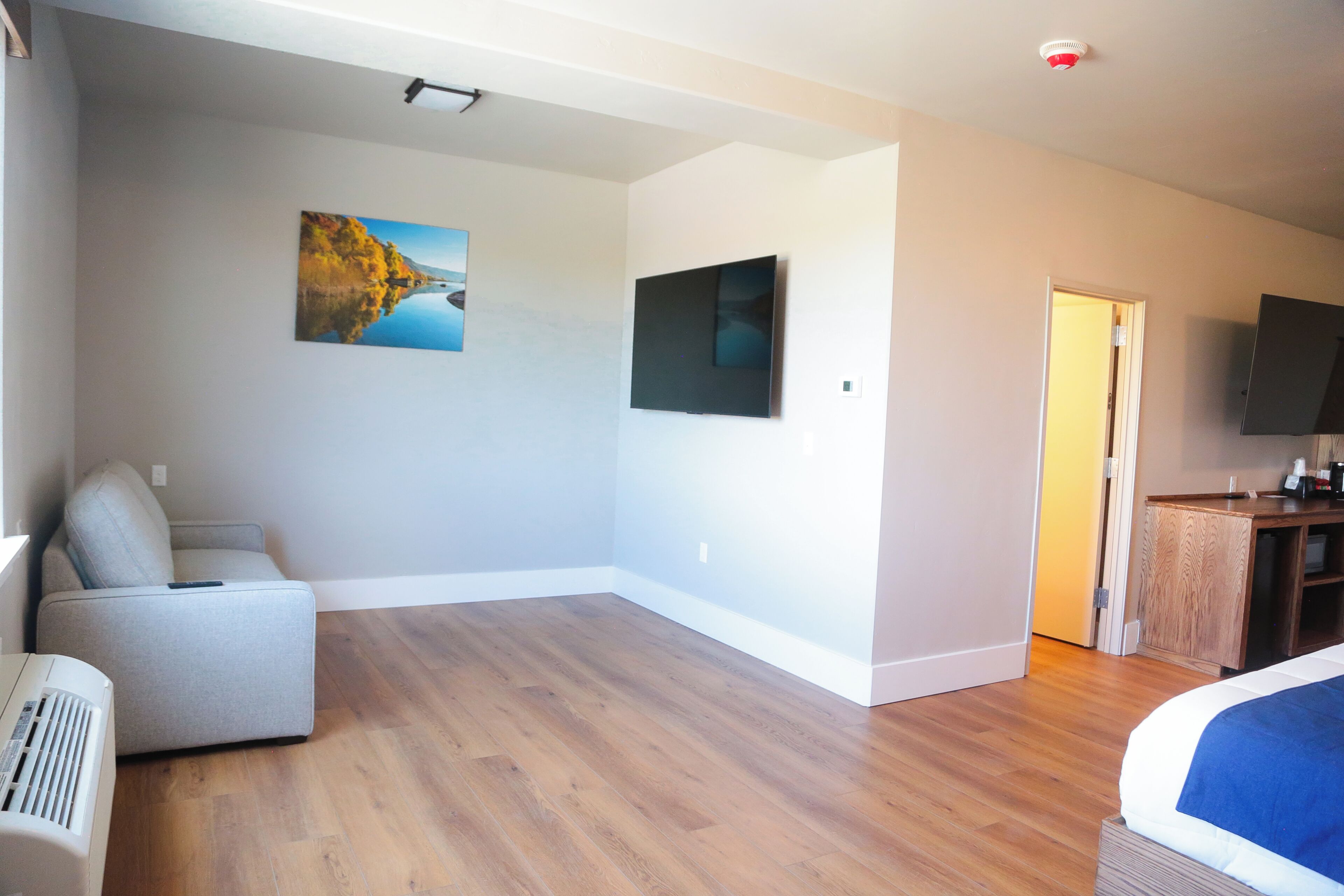 Een ruime kamer met een groot bed, een bank, een flatscreen televisie aan de muur en een landschapschilderij.