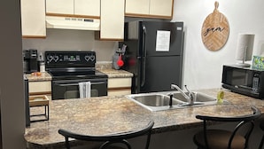 A kitchen with a granite countertop, a black refrigerator, a stove, and two bar stools.