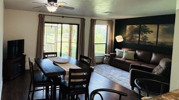 A dining area with a table and chairs, a sofa, a TV, and a ceiling fan.